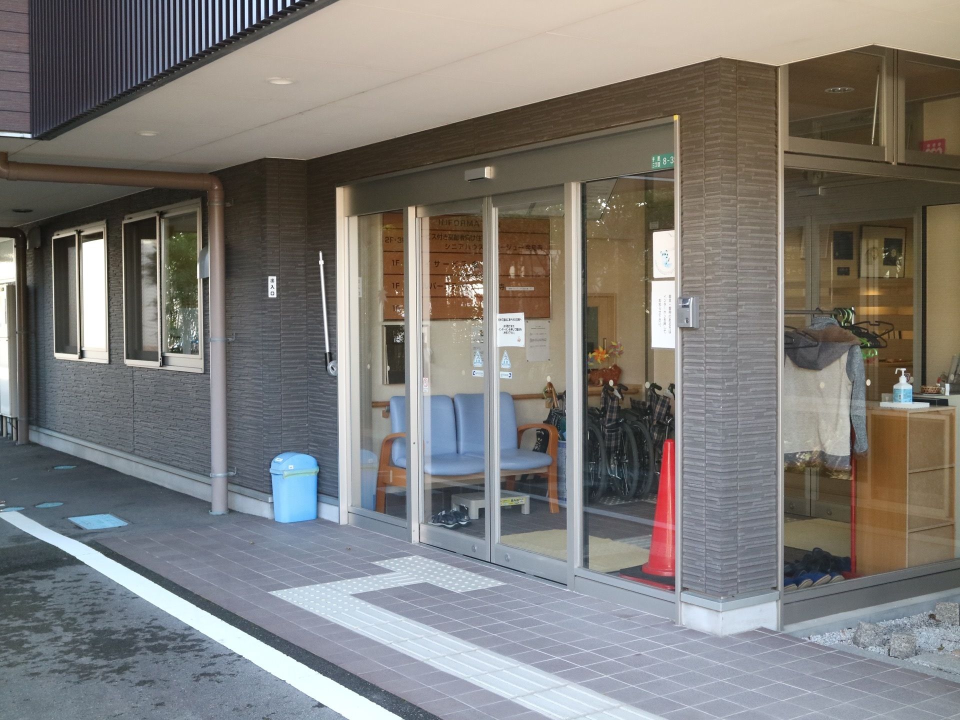 玄関前にはひさしがあり、扉の前まで点字ブロックが設置されている。扉の内部に、車椅子が折りたたんだ状態で置かれている。