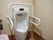 共用トイレに男性用便器が設置されている。便器を取り囲むようにして手すりが取り付けられている。感知式水洗である。