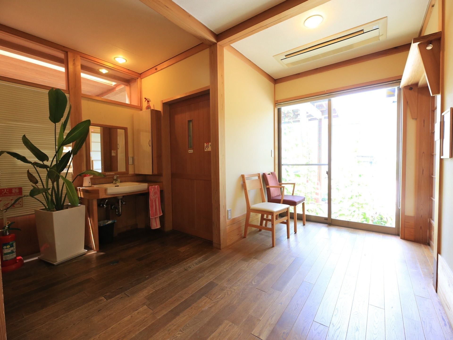 空調設備が整った廊下で、大きな窓からは外光が差し込む。洗面台の横には、消火器や観葉植物が置かれている。