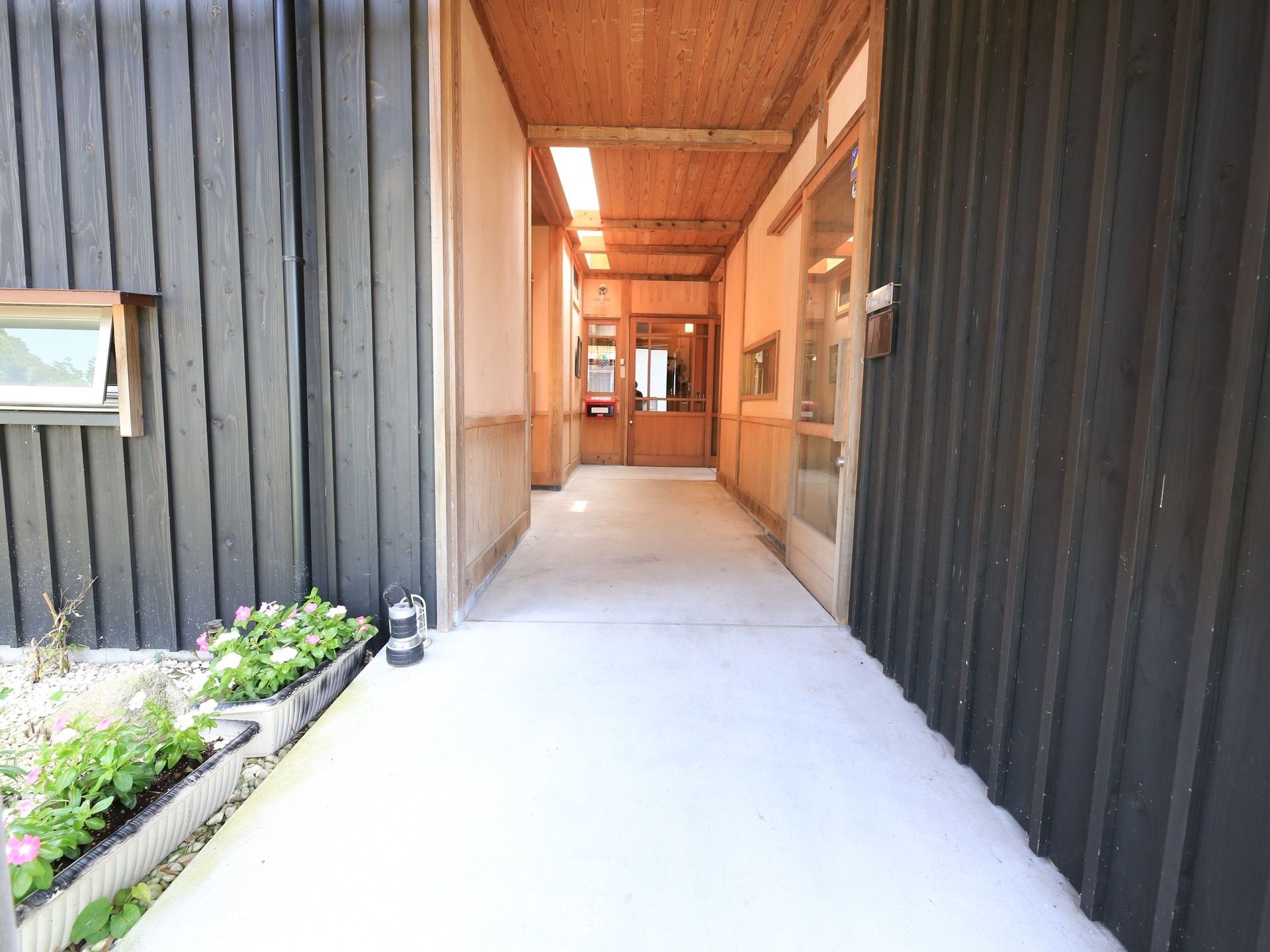 玄関前で撮影された通路の写真である。手前には、植物が植えられた複数のプランターが並べられている。