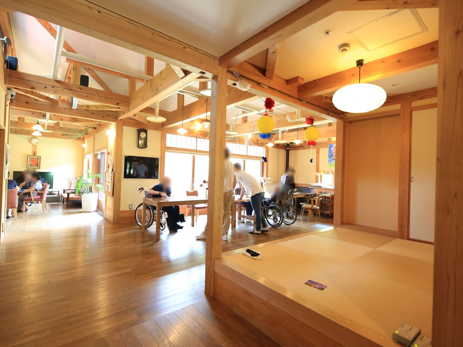 通路途中に食堂やリビングが設けられており、スタッフや入居者様が集まっている。手前には小上がりの和室がある。