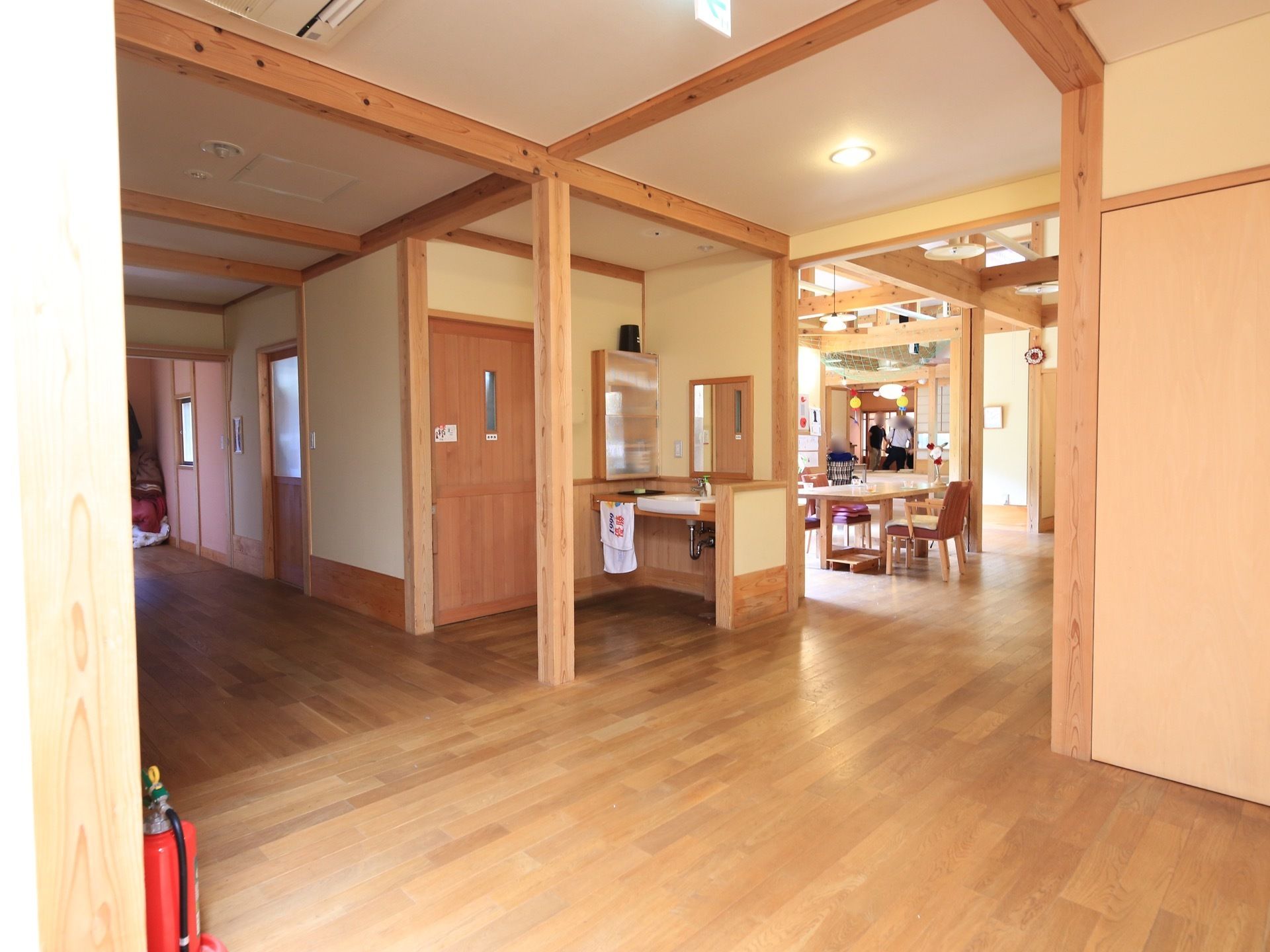 ゆとりある見晴らしの良い廊下で、途中に共用のトイレと洗面台が配置されている。奥にはリビングスペースが見える。
