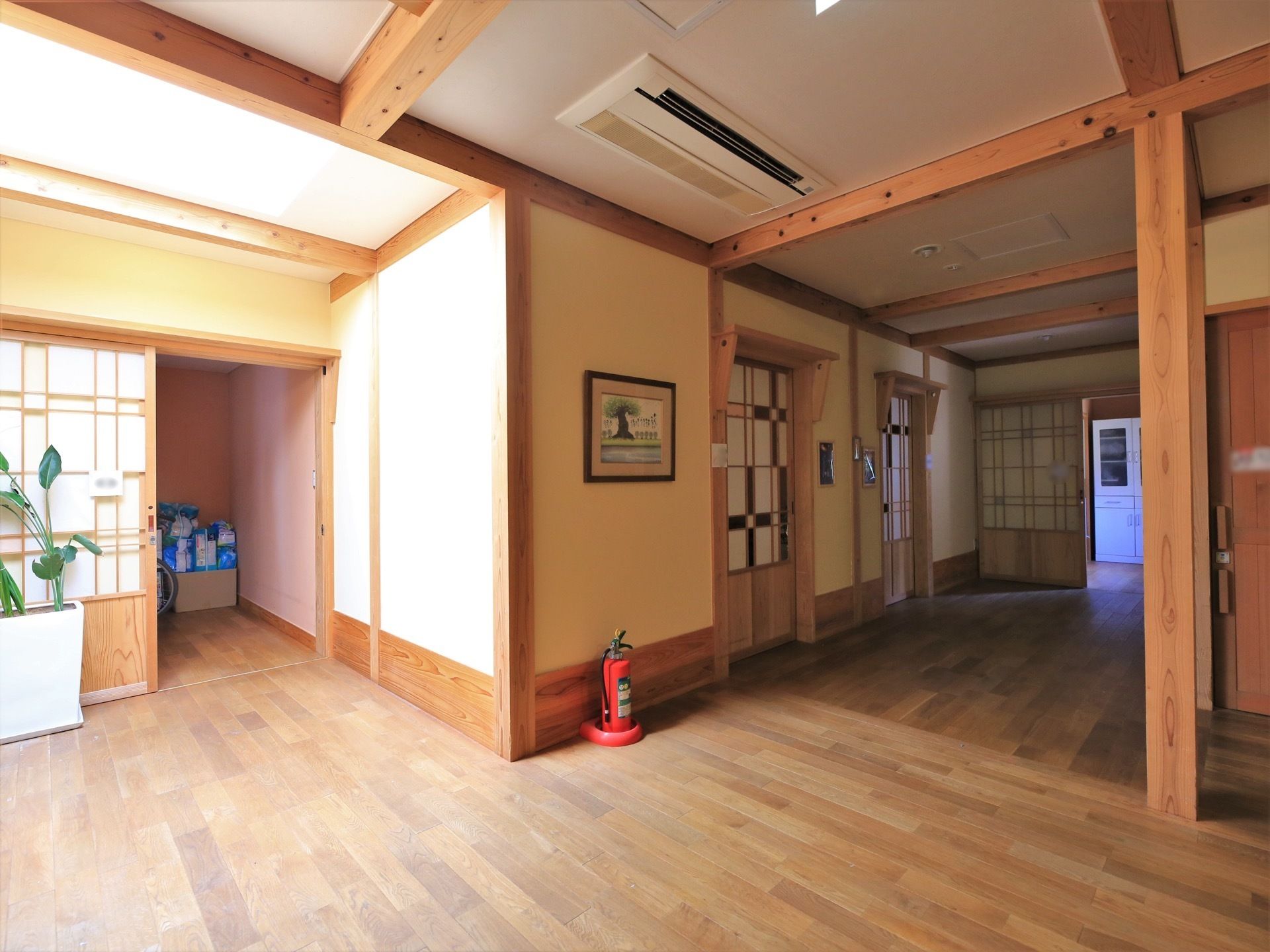 居室前の開放的な廊下で、各入口はデザイン性のあるスライド式の扉となっている。横の壁には、絵が飾られている。