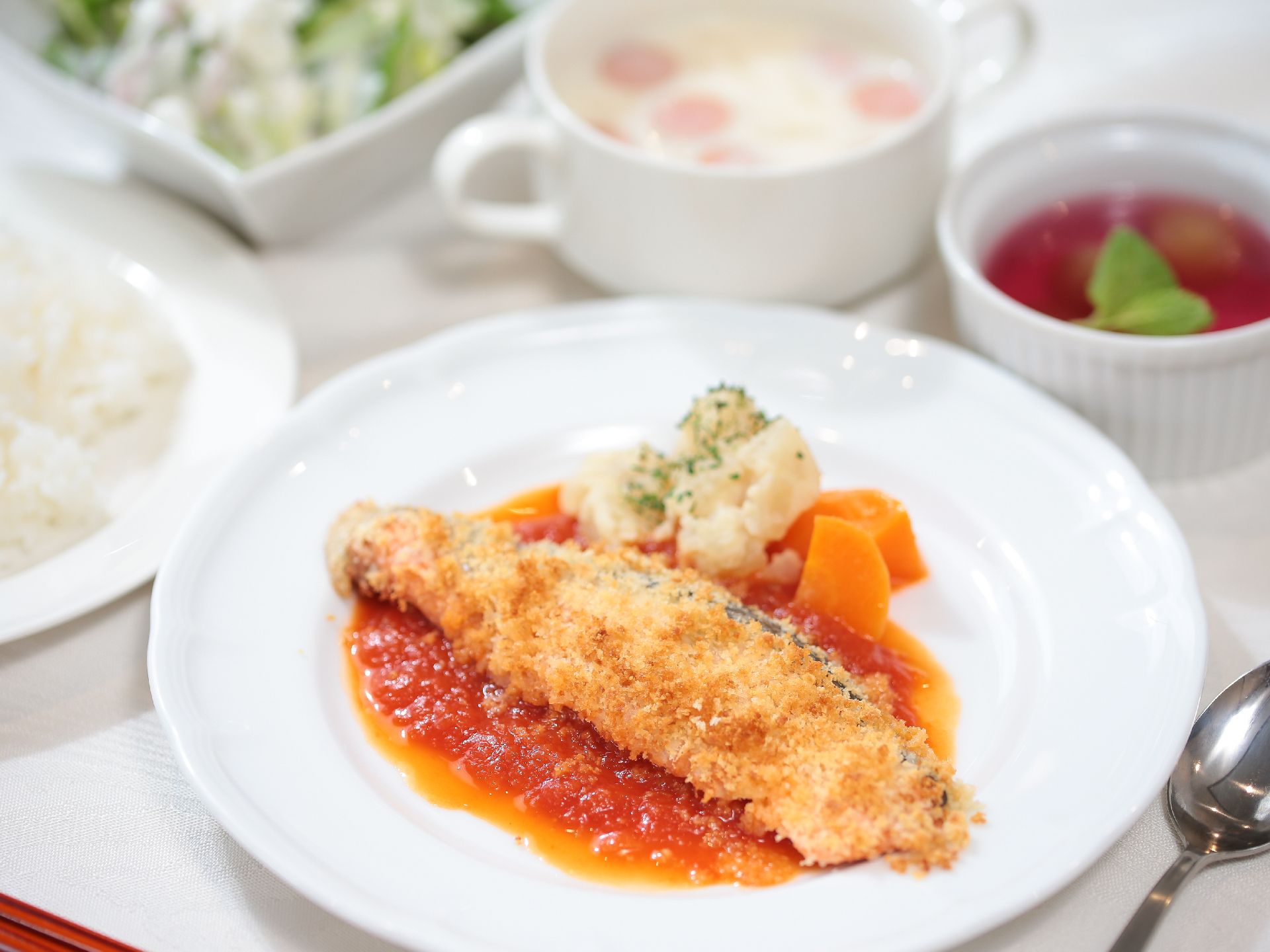 白いテーブルクロスのかかったテーブルの上に、洋食メニューの食事が並べられている。メインは魚料理となっている。