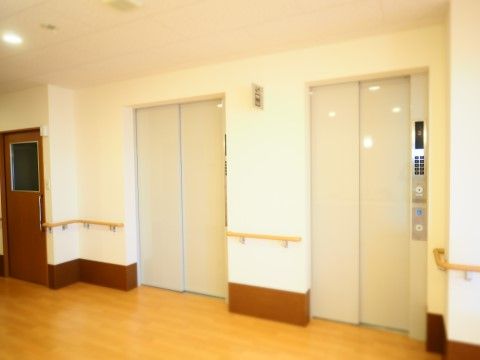 白い壁、明るいフローリングの床。エレベーターが２基あるので、待ち時間が短くてすむ。手すりも設置されている。