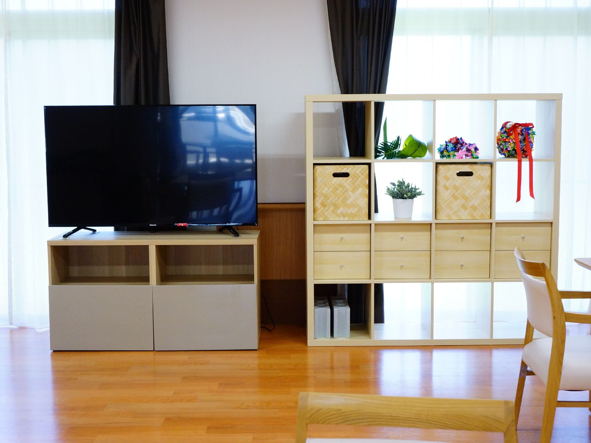 くつろぎスペースには大きなテレビがある。お洒落な棚が設置してあり収納の入れ物や飾り、観葉植物があるおしゃれな空間。
