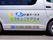 シルバーの社有車の側面には、運営会社の愛称・ロゴ・連絡先が表示されている。施設には、訪問介護やデイサービスといった併設サービスがある。