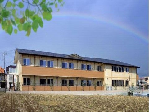 虹がかかる青空の下、目の前に広い畑がある２階建ての施設