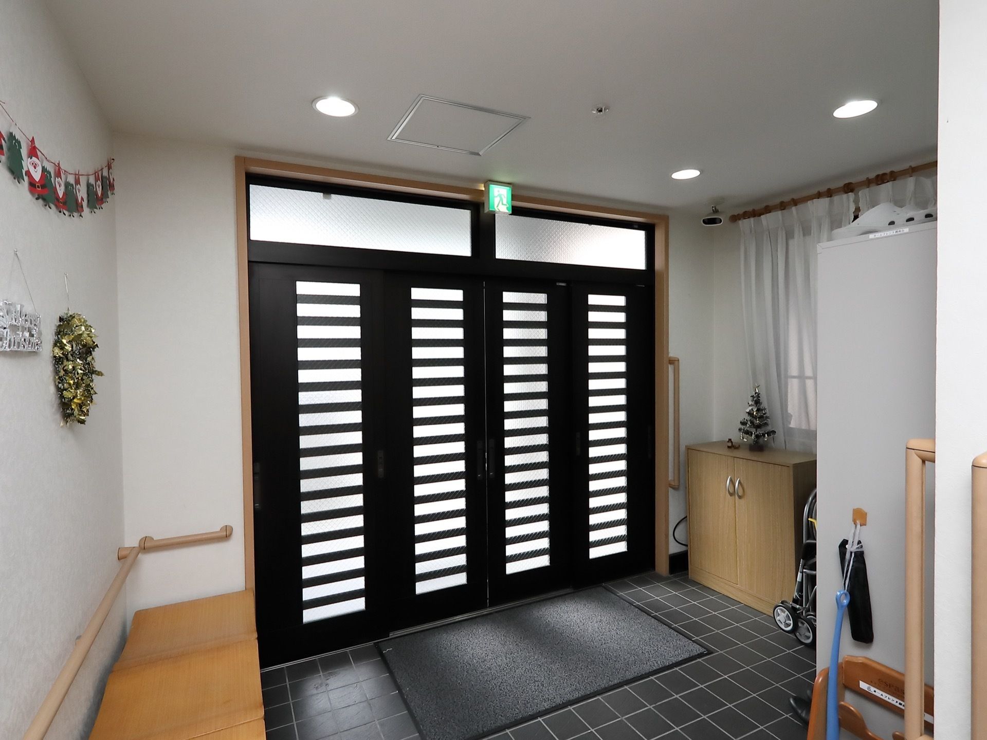 出入り口は大きな黒い引き戸になっていて、上には誘導灯が設置されている。左側には木目調のベンチが置かれており、壁には手すりがついている。