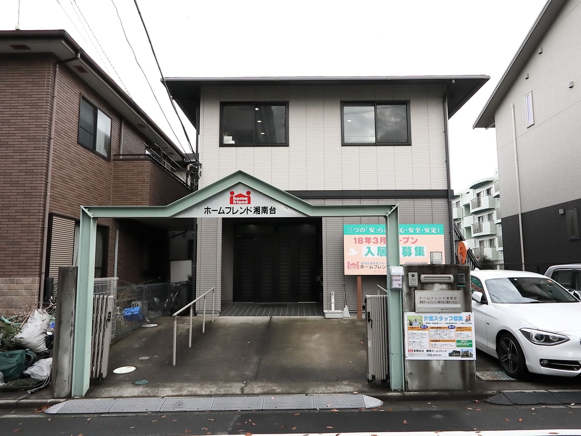 ２階建ての白い建物で、入り口のアーチの部分には施設名が書かれている。玄関前はスロープになっており、手すりが設置されている。
