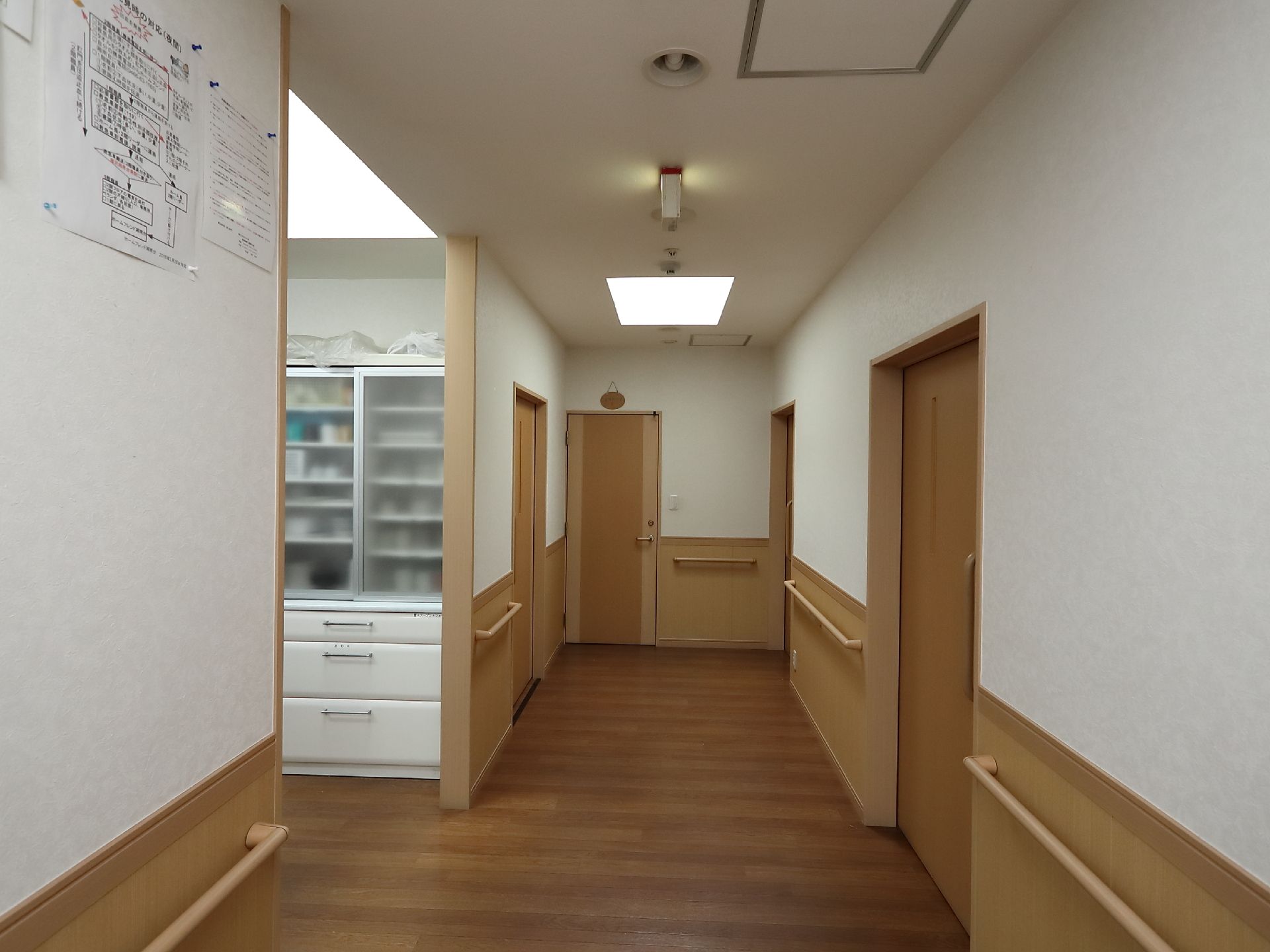 壁にお知らせの紙が貼ってあり、手すりが設置されている施設の廊下