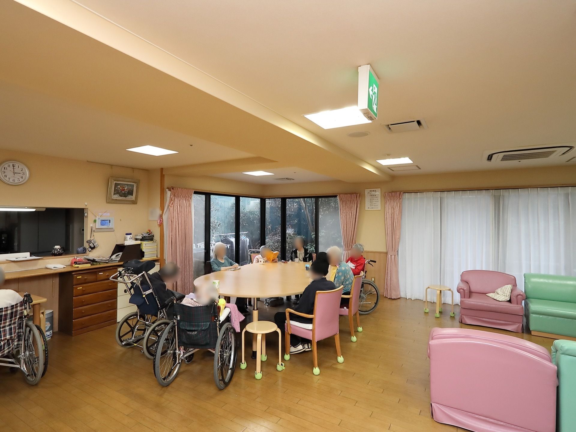大きなテーブルの周りにピンクの背もたれがついた椅子や、丸椅子が並べられている。窓にはピンクとレースのカーテンが取りつけられている。