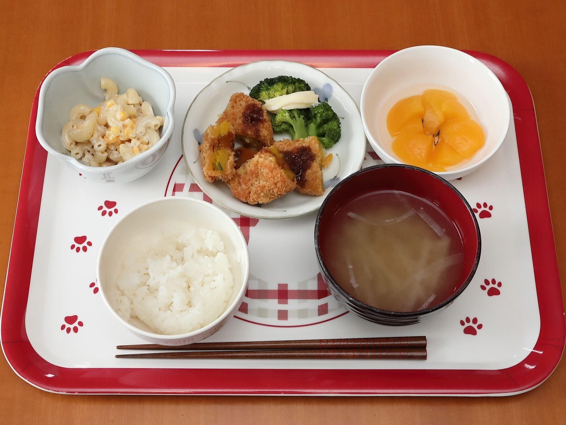 お盆の上に食事が用意されている。ご飯と味噌汁があり、そのほかに、おかずが三品とフルーツが置かれている。
