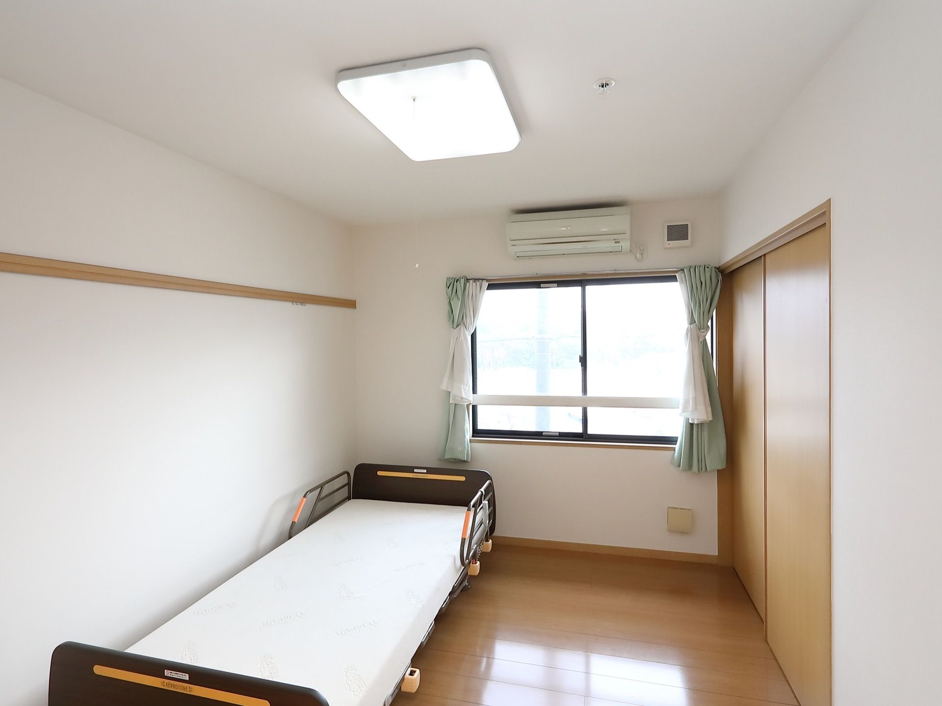 正面に窓を設けた居室である。窓の上にエアコンを完備している。壁際に、頭部側に柵のついたベッドを設置している。