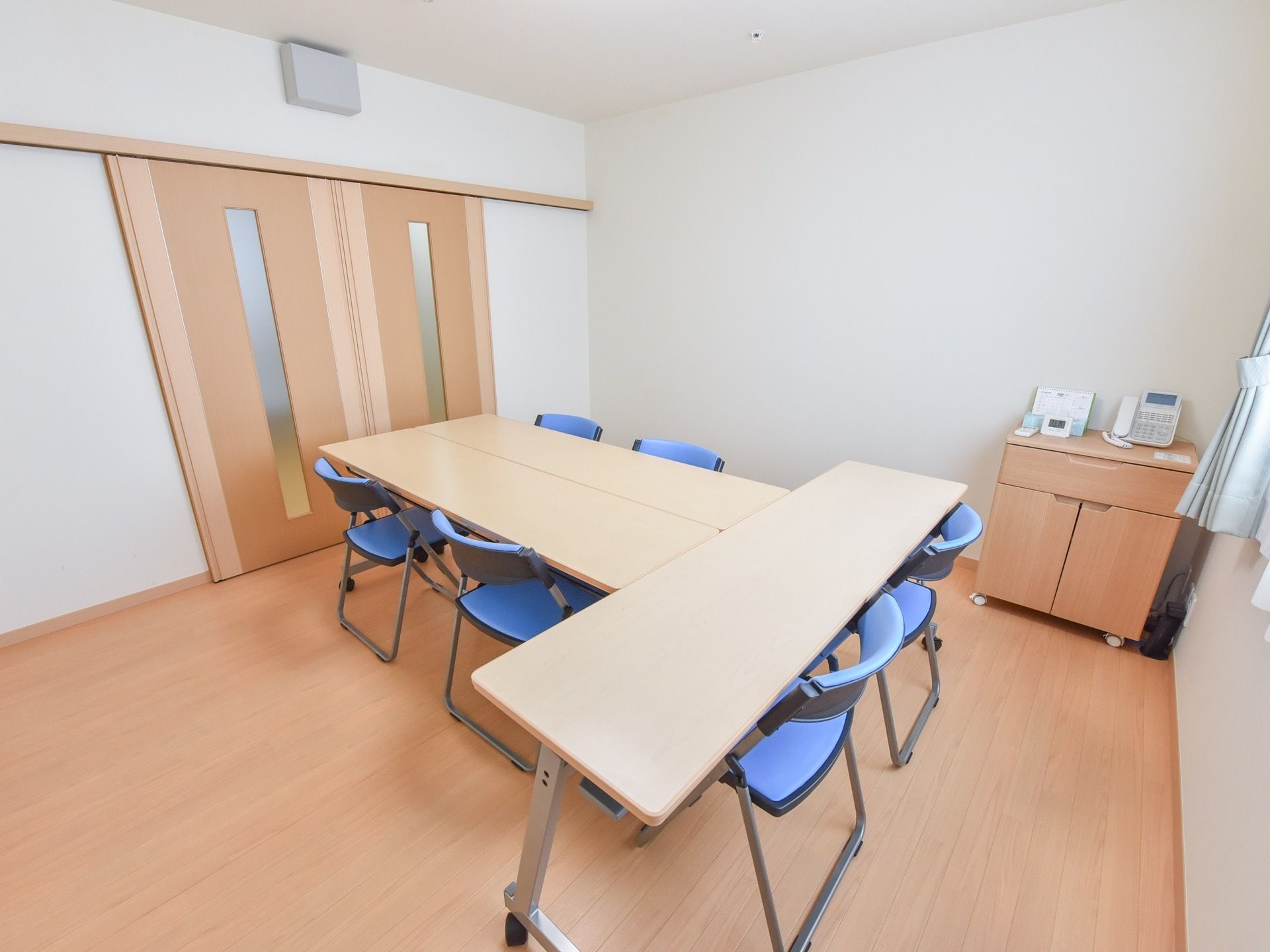 両開き扉や窓が設置され、明るい木目調を基調に整えられた相談室である。6脚の青いシートの椅子が印象的である。