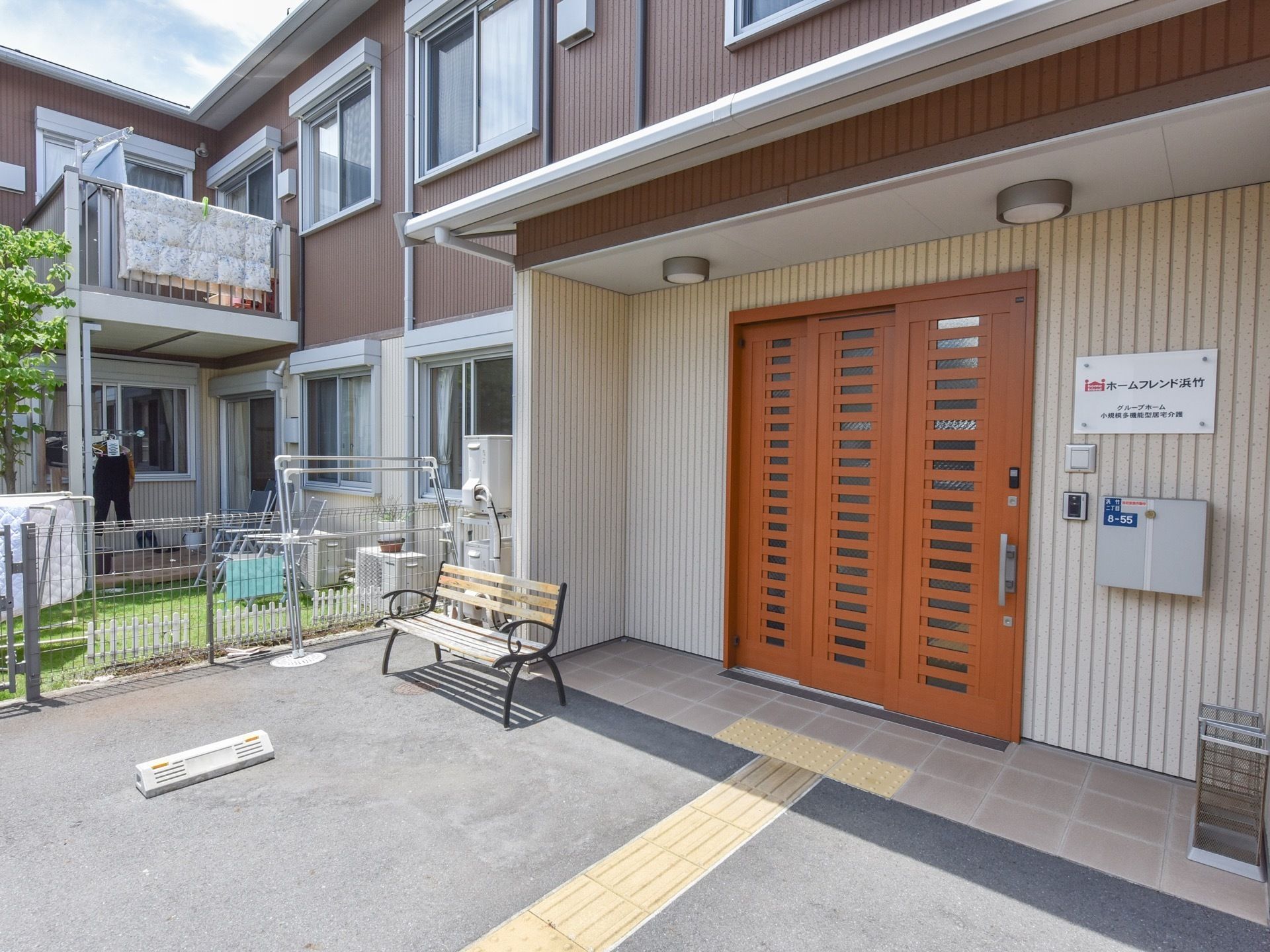 施設入口は、間口の広い片開き扉が設置されている。壁には、施設名称のプレートやインターホンが取りつけられている。