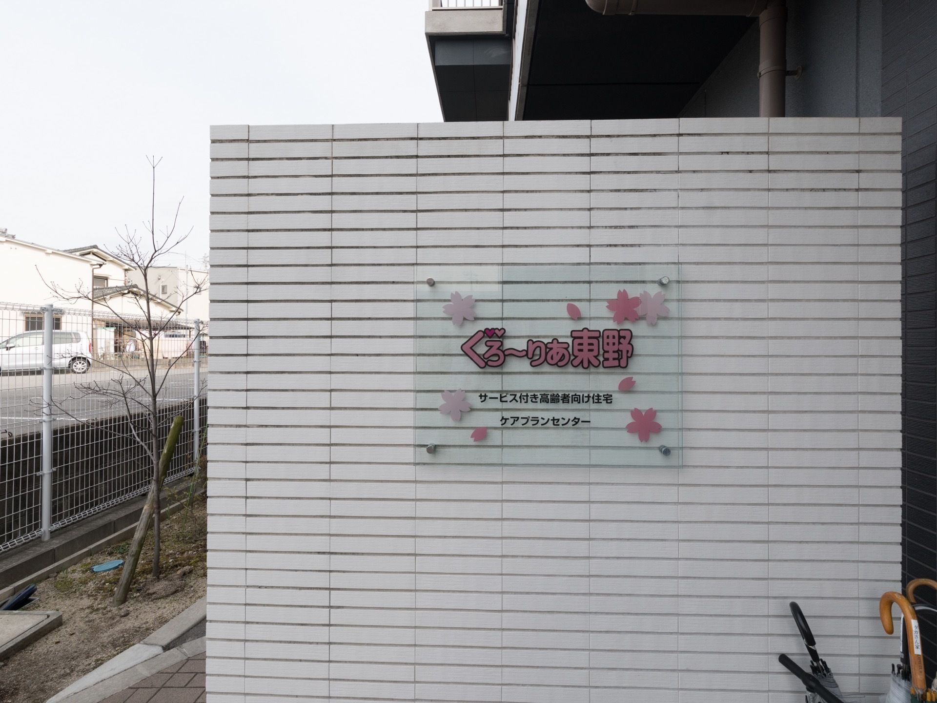 エントランスに設置されている木製の白い衝立に、施設名が書かれた透明なアクリルの看板が取り付けられている。