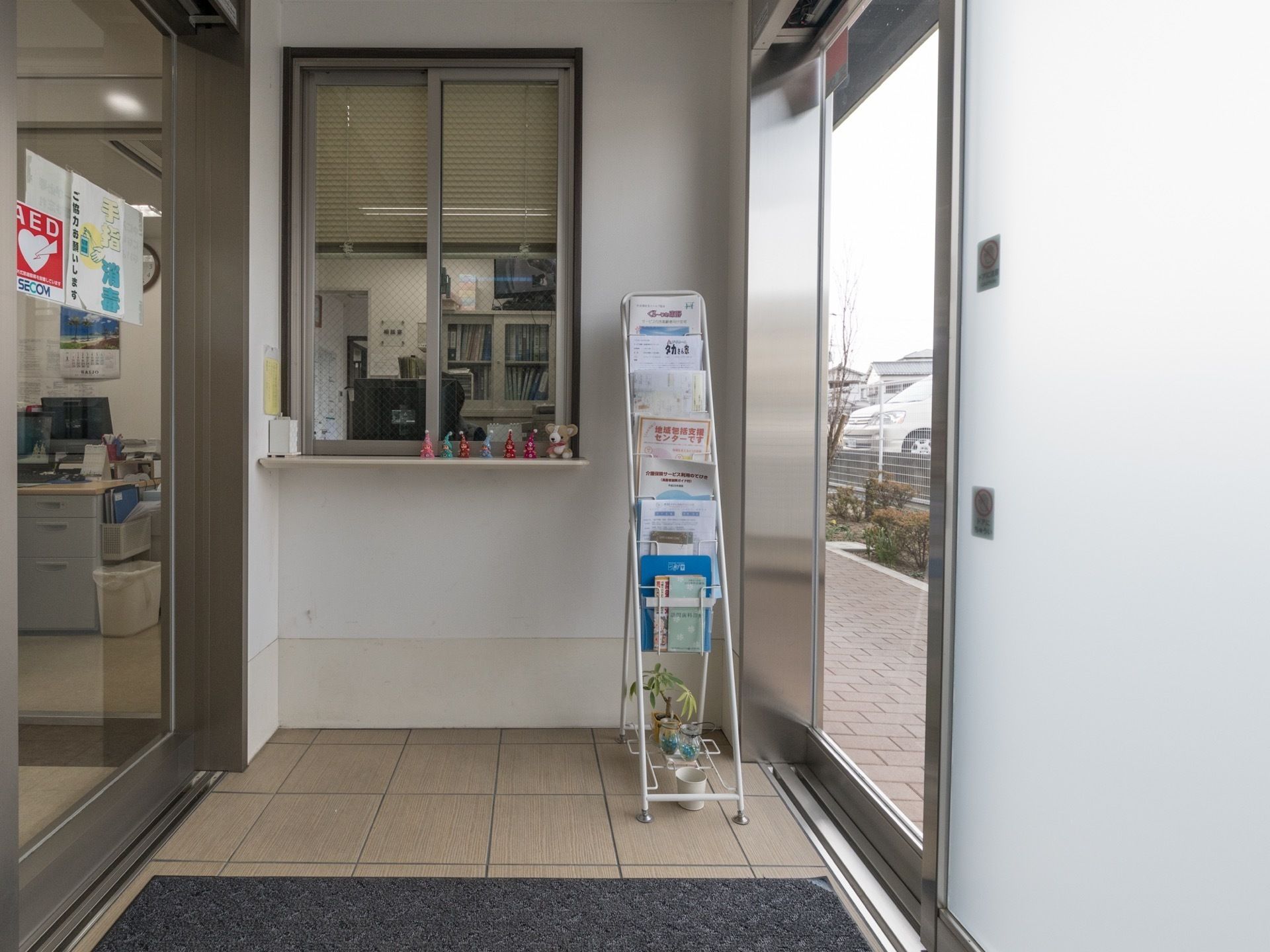 エントランスには風除室があり、受付カウンターを備え付けている。またフロアにはパンフレットがあり、マットが敷かれている。