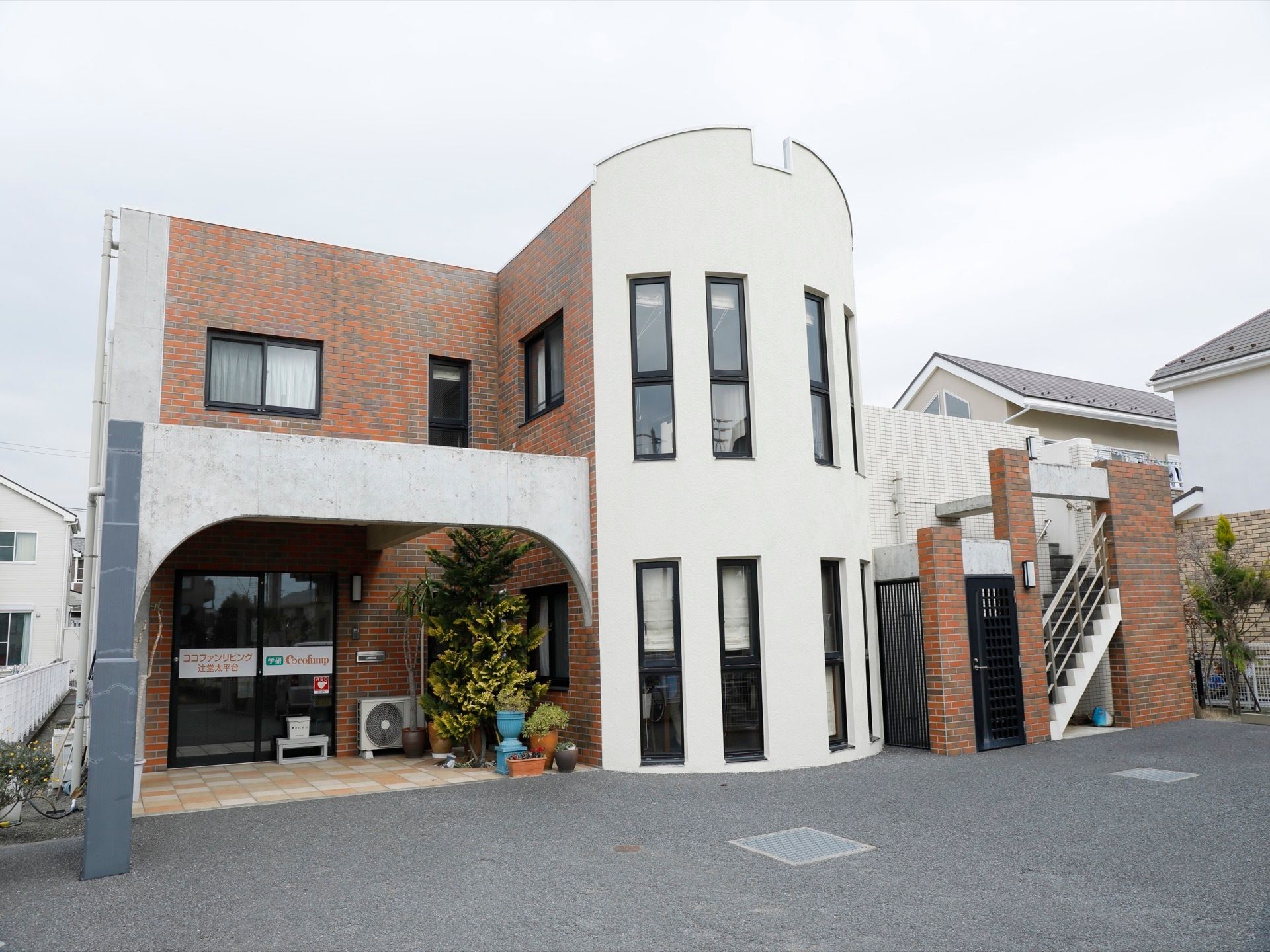 足元はバリアフリーになっている。玄関は自動ドアで、近くに背の高い植木が置かれている。２階へと続く外階段もある。