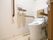 便器に背もたれ付きの跳ね上げ式手すりが、装備されたトイレである。壁には、呼び出しボタンや温水洗浄便座用リモコンが設置されている。