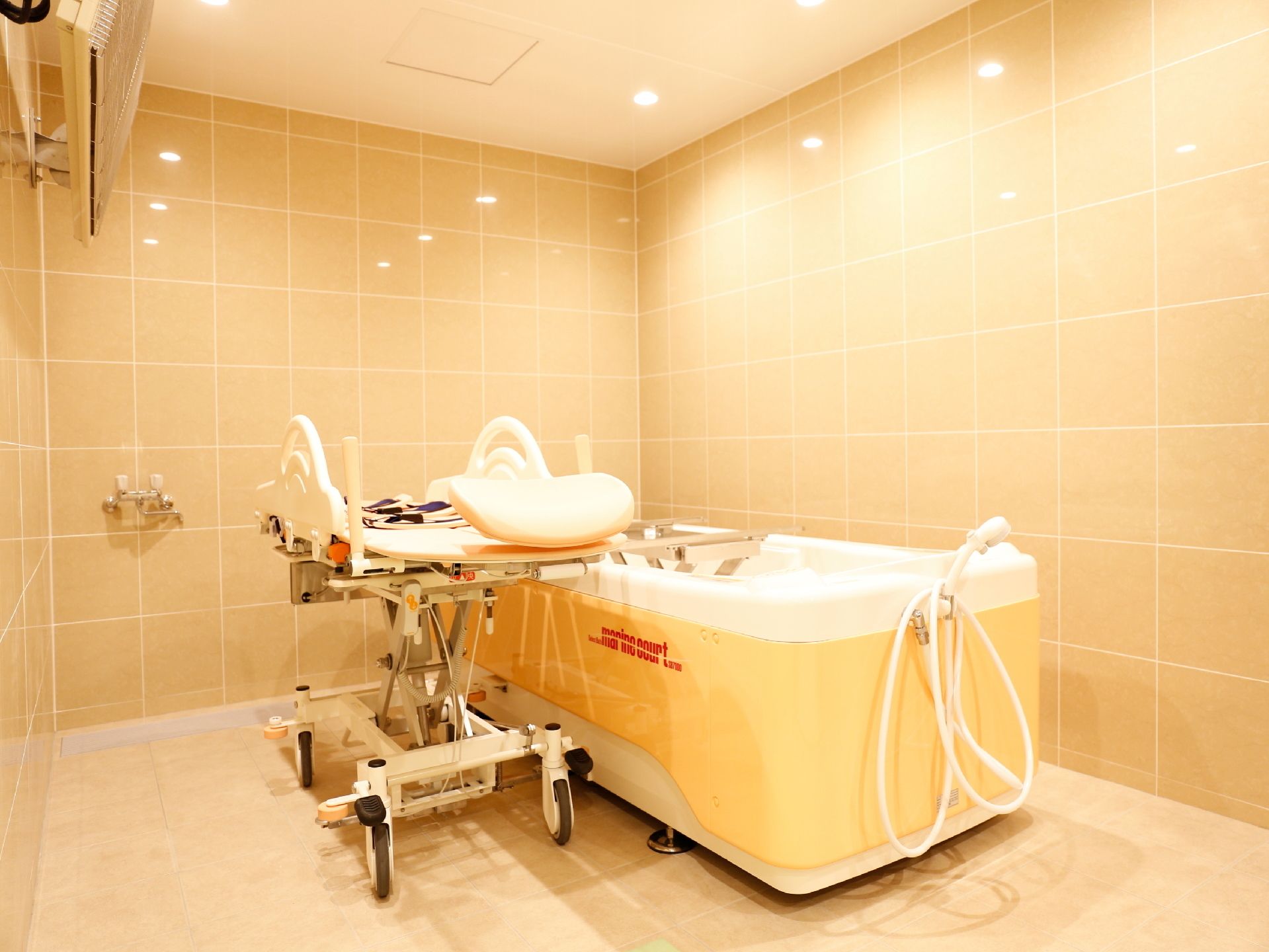 介護用浴室は壁も床も天井もベージュ色でやさしい雰囲気である。身体を横にしたまま入れる大きさの浴槽とストレッチャーがある。