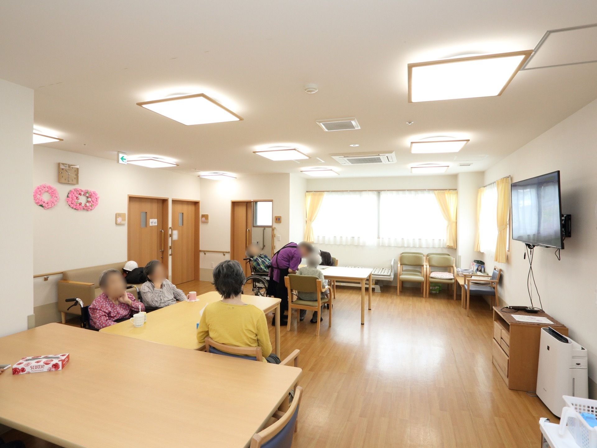 壁に時計が掛けられており、近くに紙で作った花の飾りがある。窓にはレースとイエローのカーテンが掛けられている。