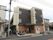 建物３階建てで幹線道路沿いにある。目の前にはバス停があり、自動販売機とベンチが建物に沿ってある。玄関は道路から少し控えた位置にある。