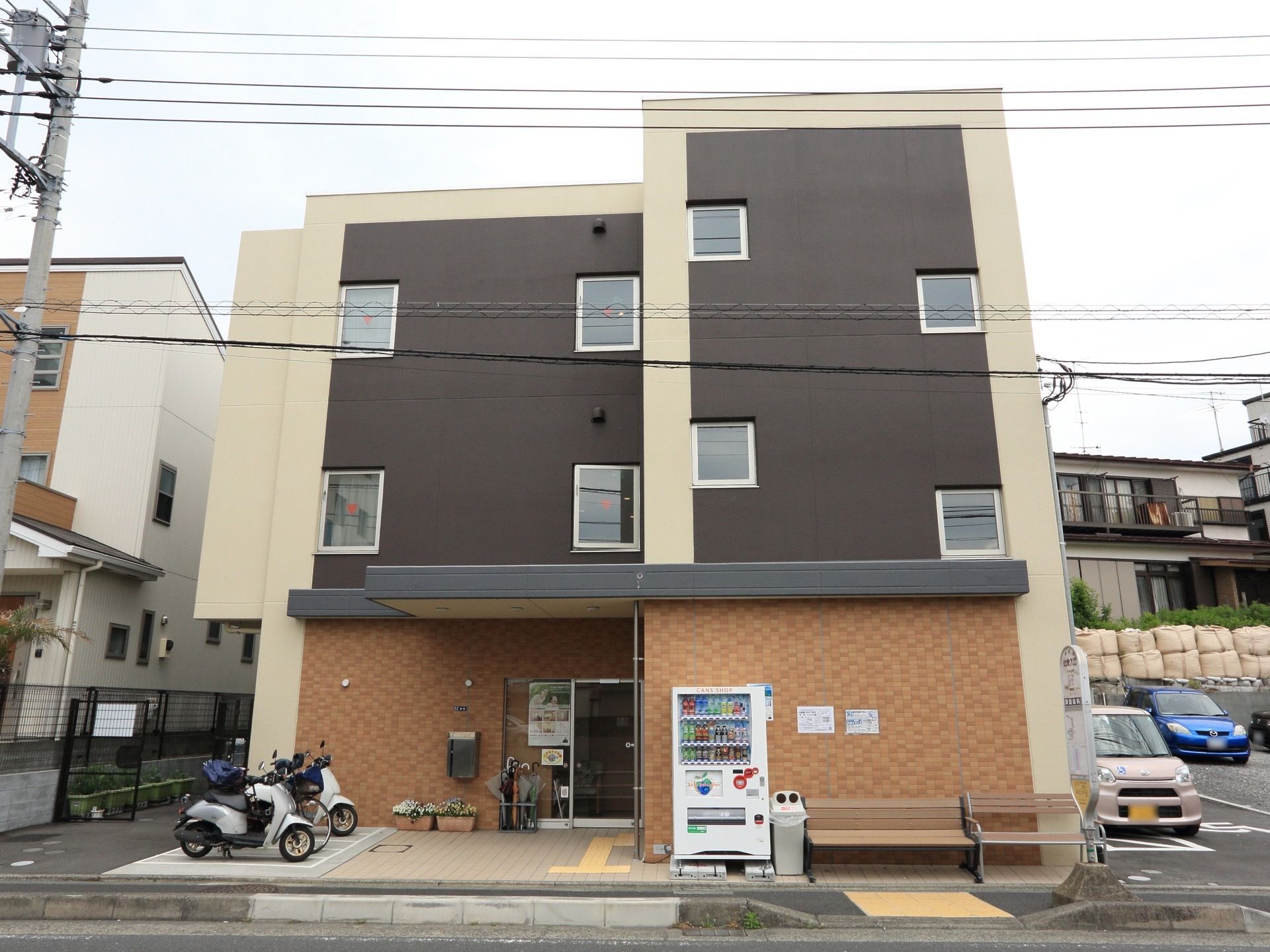 施設の建物は茶色い外壁の3階建てである。玄関を出てすぐバイクの駐輪場があり、建物の前にはバス停がある。右手には駐車場が完備されている。