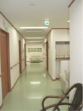廊下には茶色い居室のドアが並んでいる。壁に手すりを取り付けているので、掴まりながら安全に移動できる。