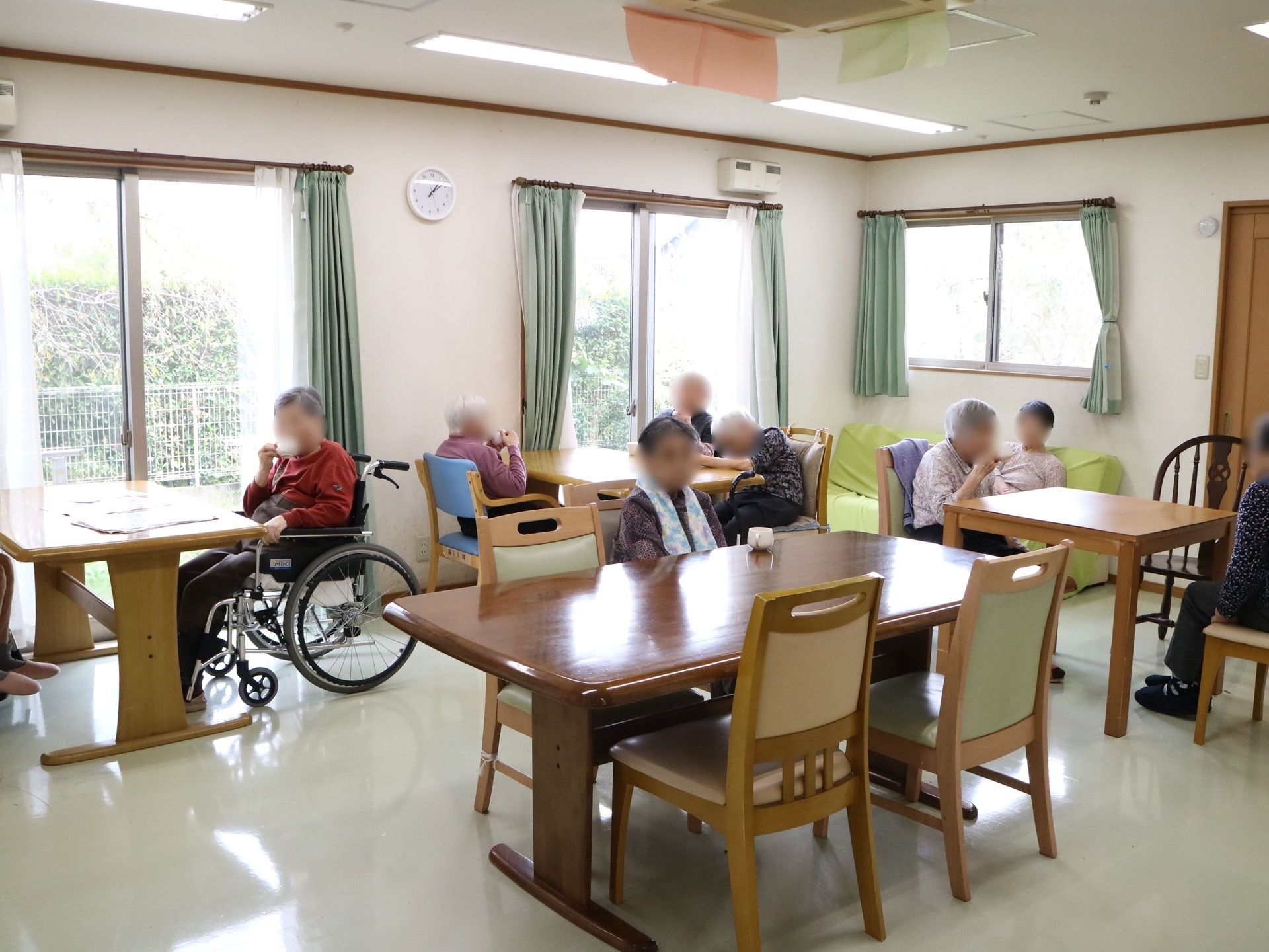 食堂に多くのテーブルや椅子が置かれている。入居者様が思い思いの場所に座って、お茶やコーヒーを飲んでいる。
