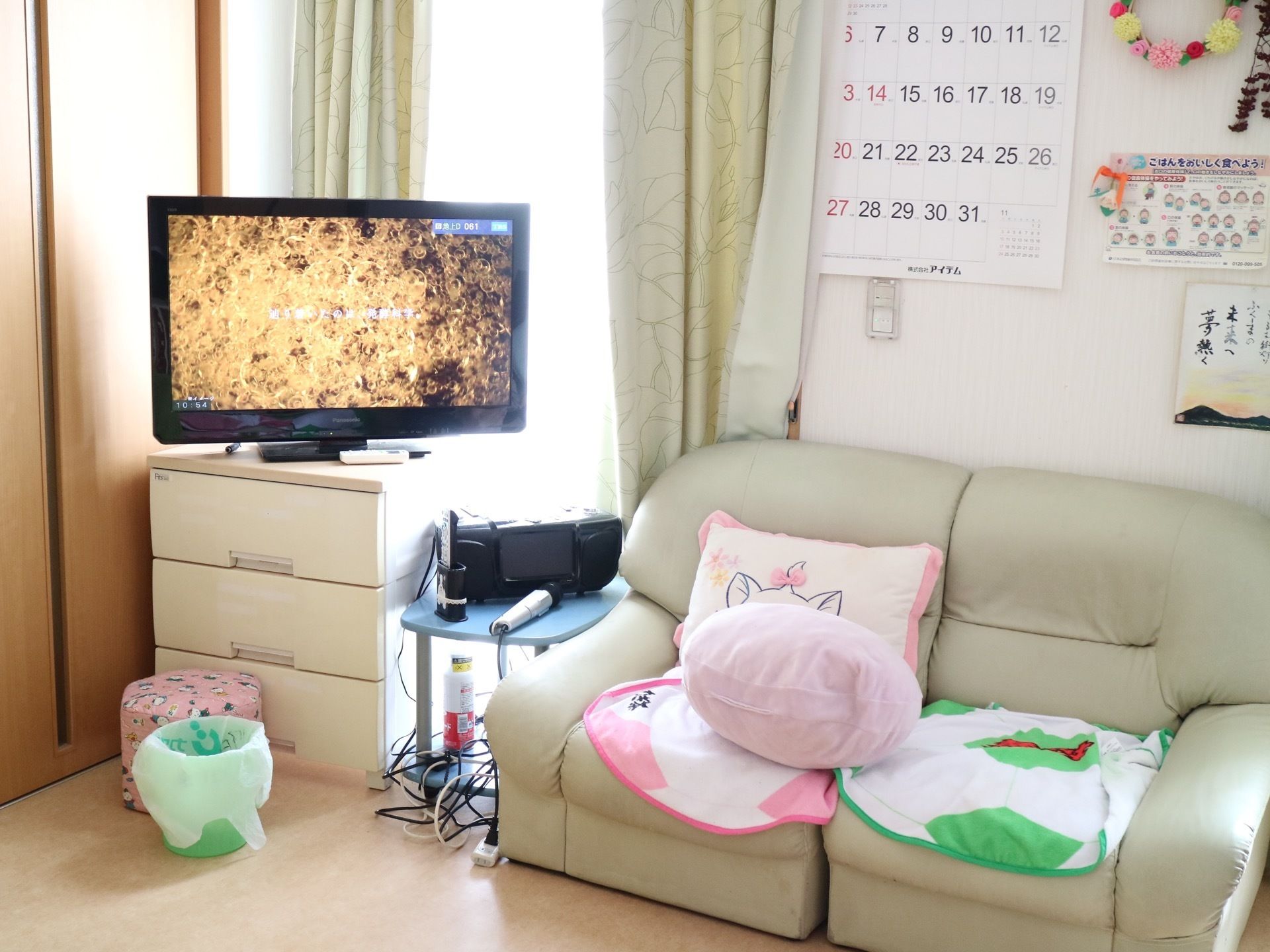 リビングにはソファーが置かれている。テレビが設置されており、カラオケの機材が用意されている。壁にはカレンダーが飾られている。