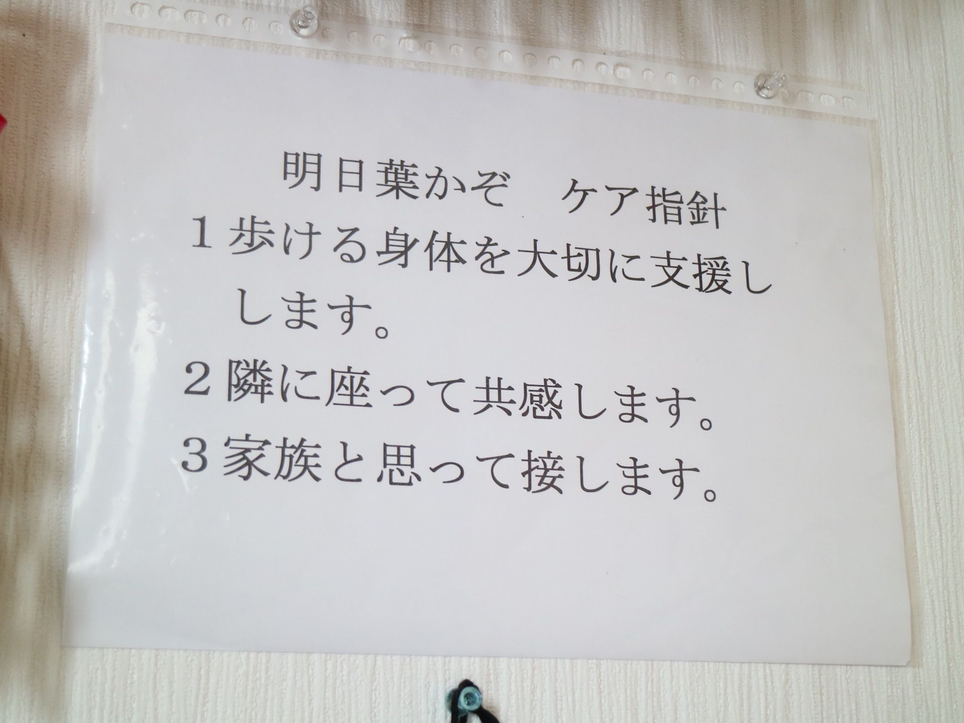 白い壁に、クリアファイルに入れられた紙が掲示されている。紙にはグループホームのケア指針が書かれている。