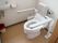 便座の両側に手すりがあり、背もたれの付いたトイレがある。戸は木目調の引き戸で、中には洗面台も付いている。