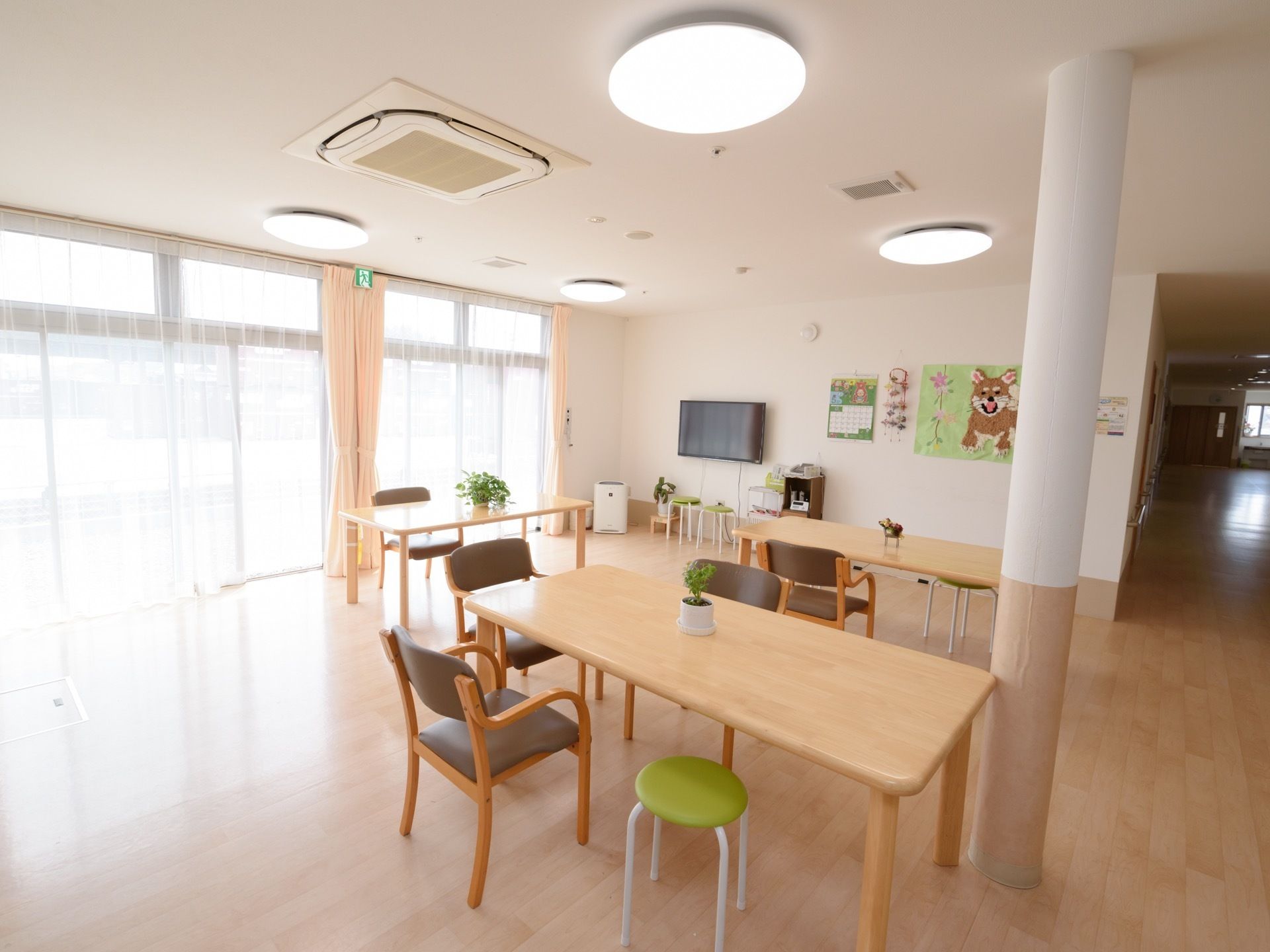 明るく開放的な空間に、ゆとりをもってテーブルが配置されている。テレビや空気清浄機などの設備がある。壁には制作された作品が飾られている。