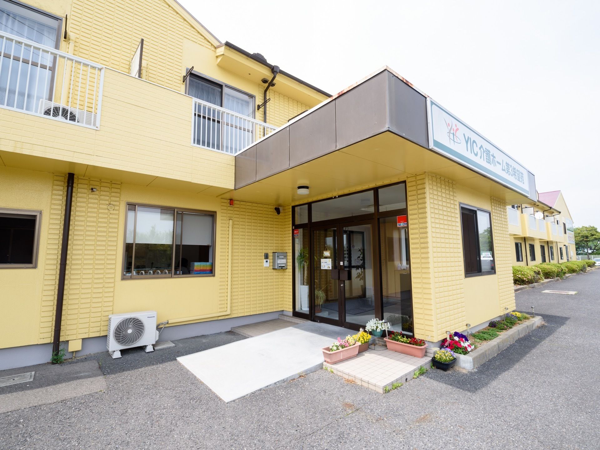 クリーム色の外壁で明るい雰囲気の建物になっている。玄関の扉の脇にはプランターがあり、花が植えられている。