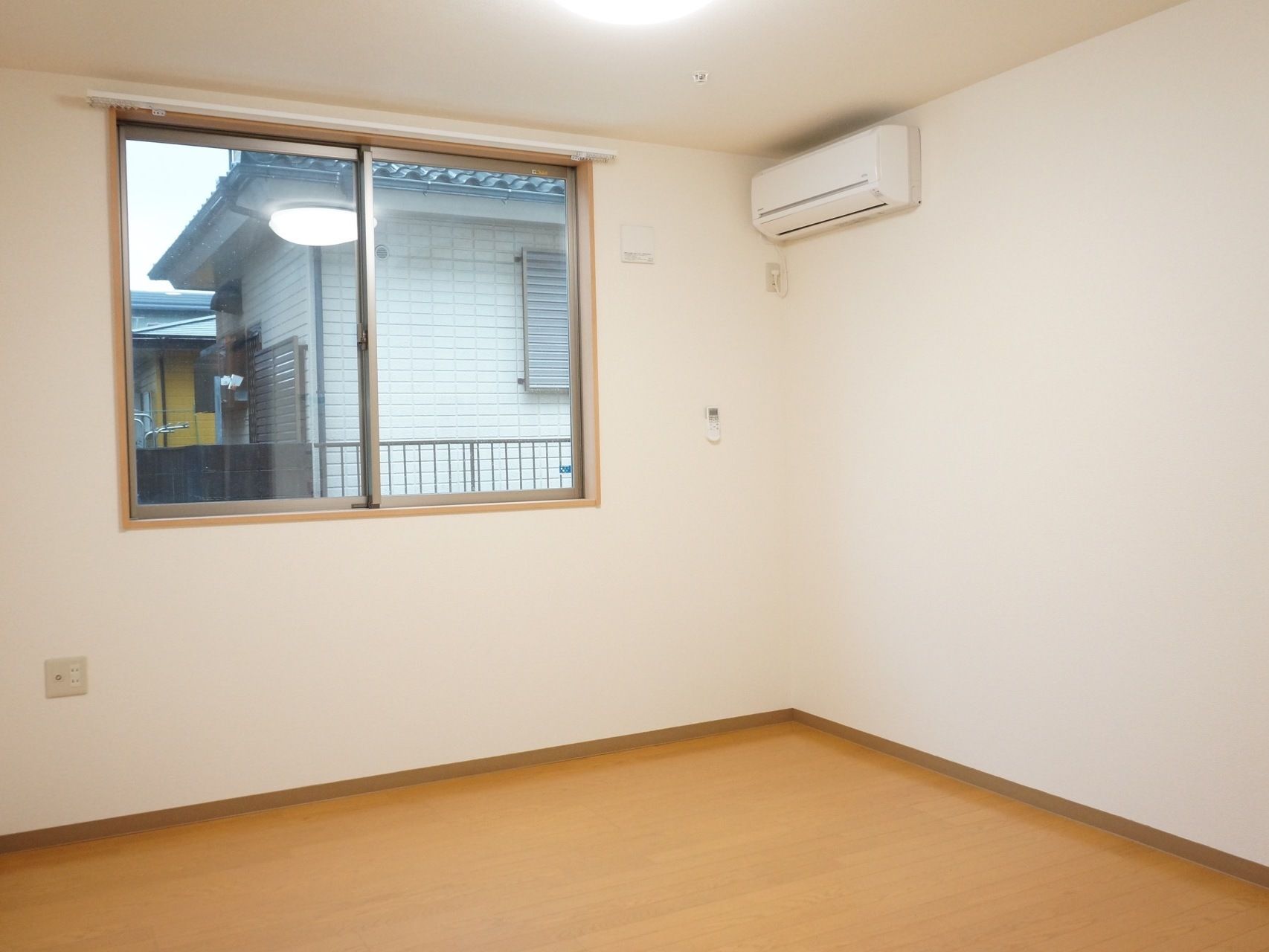 居室の壁は白く、エアコンが取り付けられている。床はフローリングである。床には家具や物は何も置かれていない。