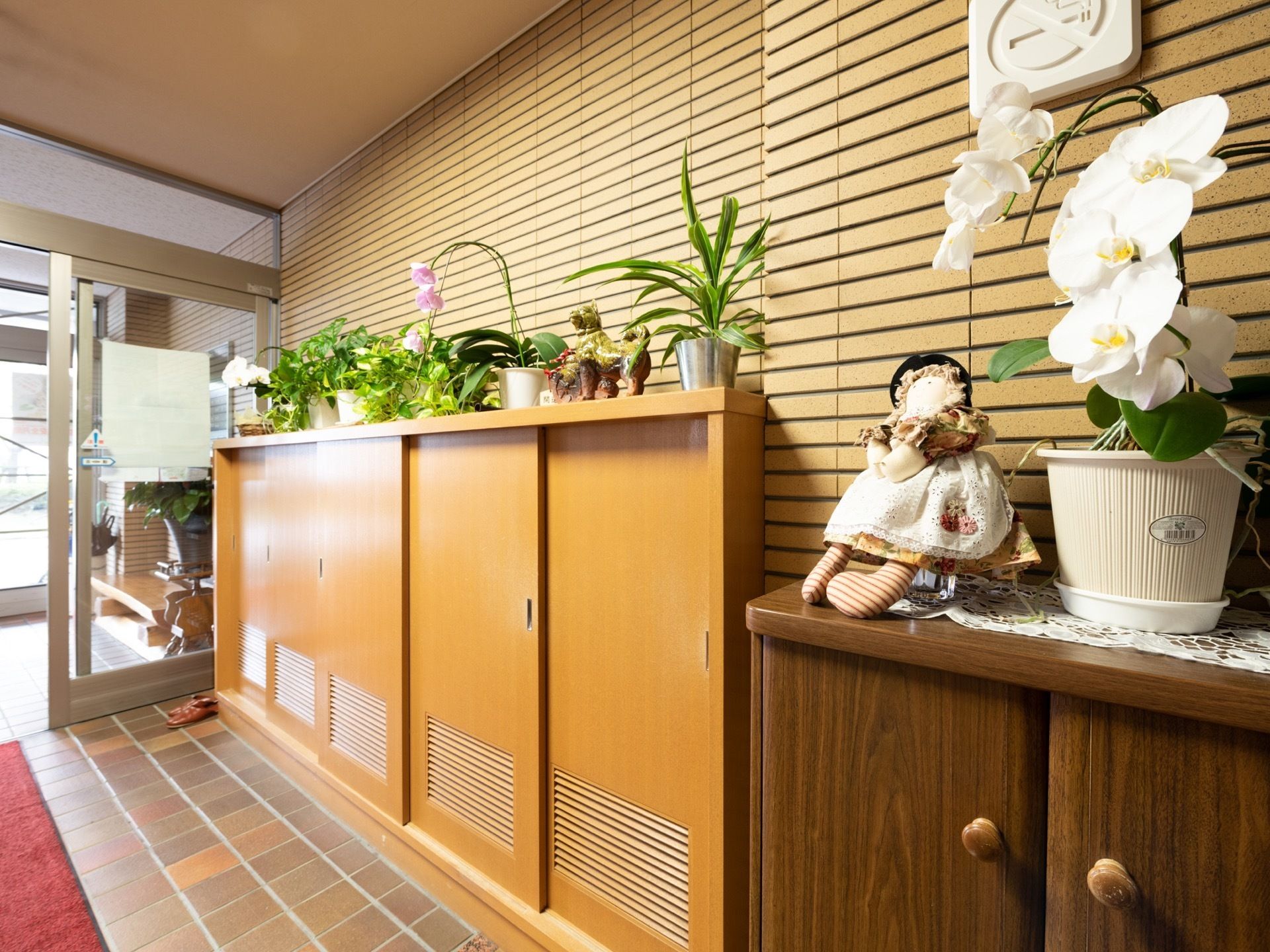 自動ドアが完備されている。玄関に引き戸式の靴箱が備えつけられており、上部には観葉植物や花が飾られている。