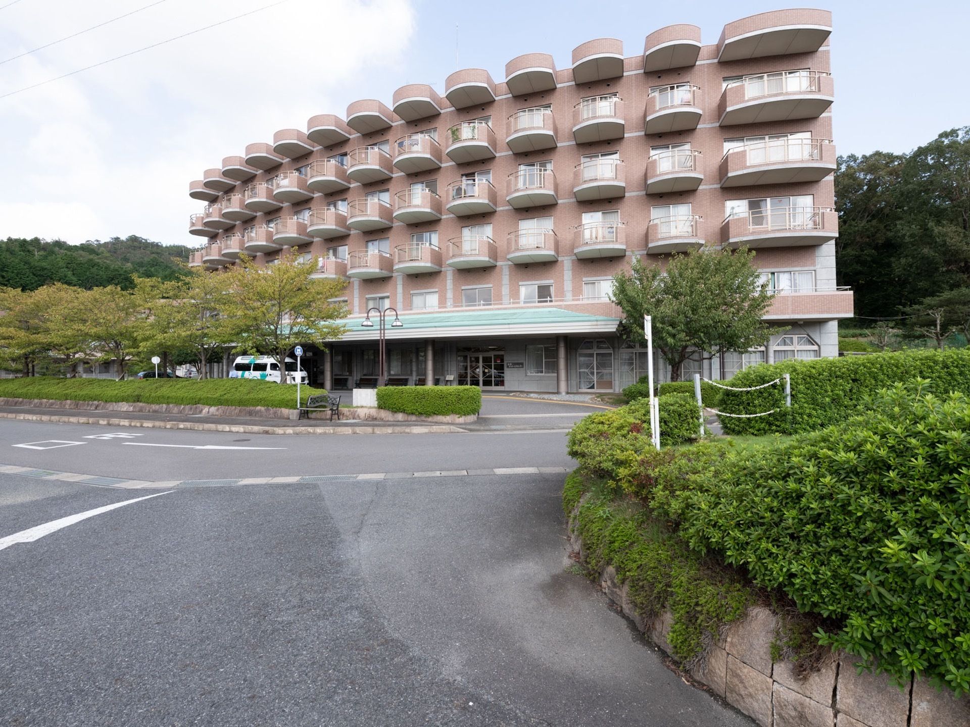 随所に緑を配置。施設の後ろには、木々が生い茂っている。地面はアスファルトで、段差がなくフラットである。