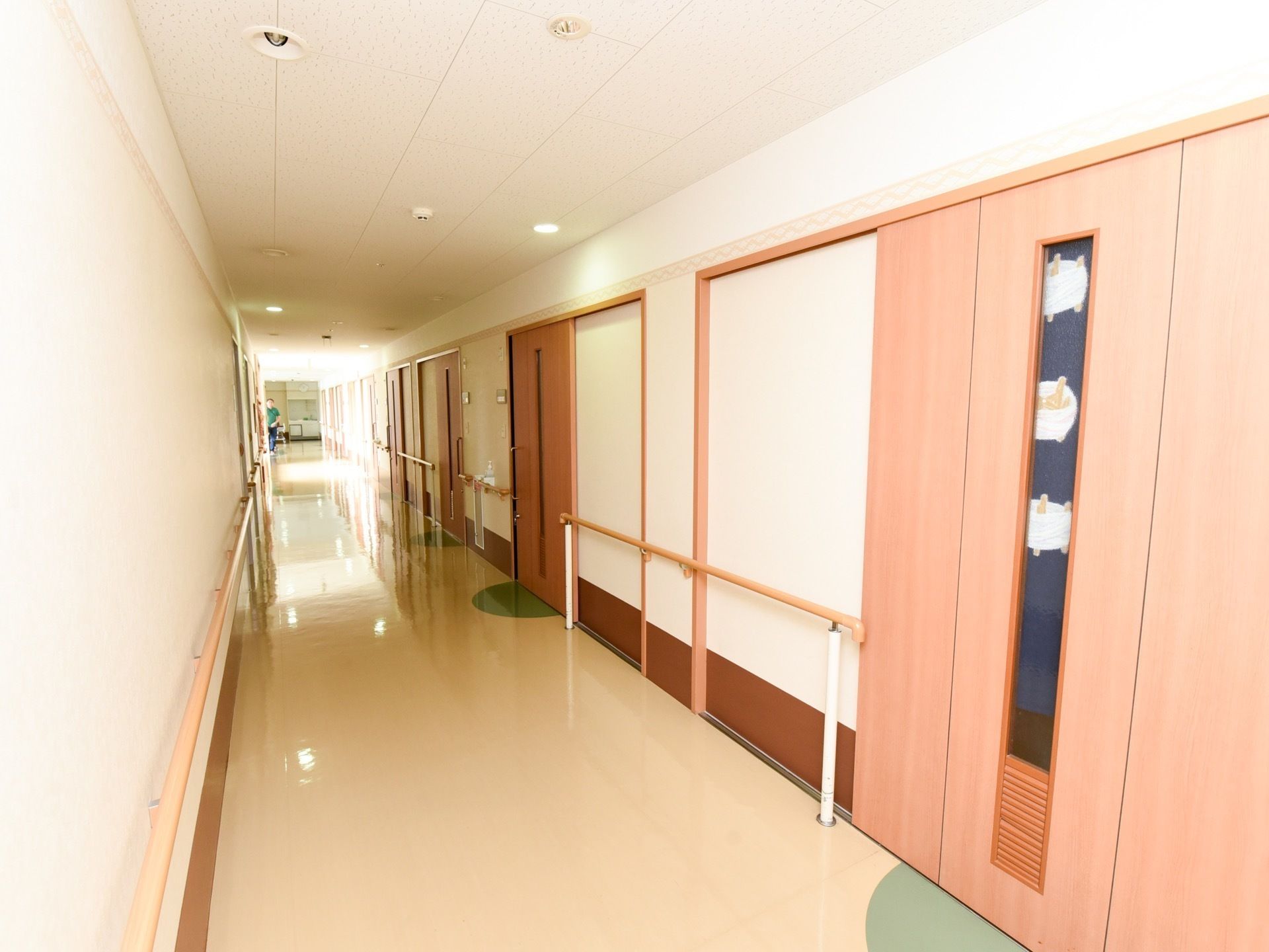 廊下の壁には長い手すりと、居室のドアが並んでいる。ドアは全てスライドドアで、ドアの横に表札が付いている。