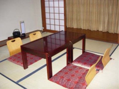 部屋の中央に小さな座卓が２つ並べられ、木製座椅子と座布団が４組置かれている。足元には畳が敷かれ、廊下との境には障子が組み込まれている。