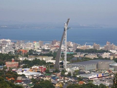 所々に木々が混ざった街並みの中に、特殊な形をした背の高い建造物がある。景色の奥には、海が広がっている。