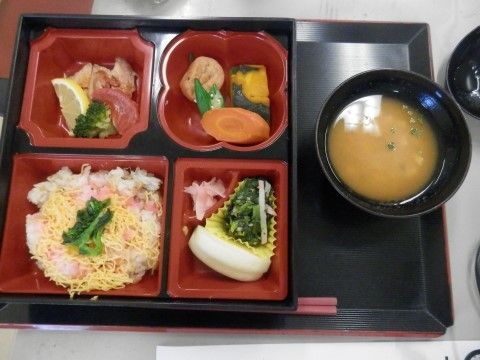 黒いお盆の上に食事が配膳されている。右側には味噌汁、左側には4つのお皿に、ちらし寿司やかぼちゃ、人参、ブロッコリーなどが入れられている。