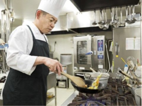 厨房で、フライパンで料理をしている、コック帽をかぶった男性