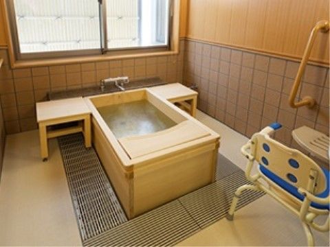 広い窓が設けられ、木製の浴槽には踏み台が付いている。シャワー設備の周辺には手すりが設置され、シャワーチェアが置かれている。