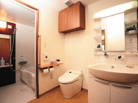 収納付きの洗面台の横に、トイレがある。手すり付きで立ち座り動作が安全に行える。奥の浴室へも段差なく進むことができる。