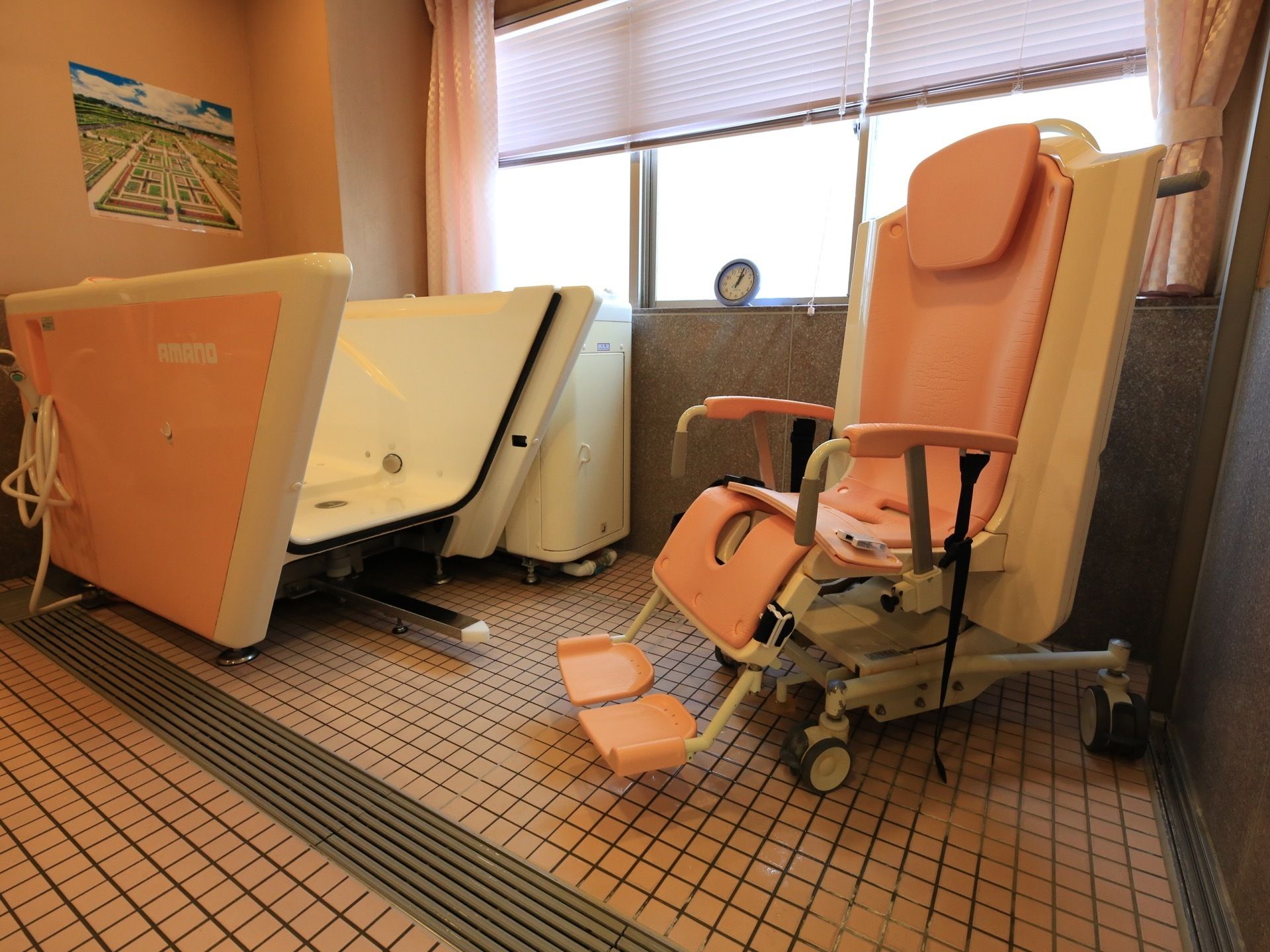 ピンク色の座って入れるタイプの機械式浴槽が１台設置されている。横には窓があり、ブラインドとカーテンが掛かっている。
