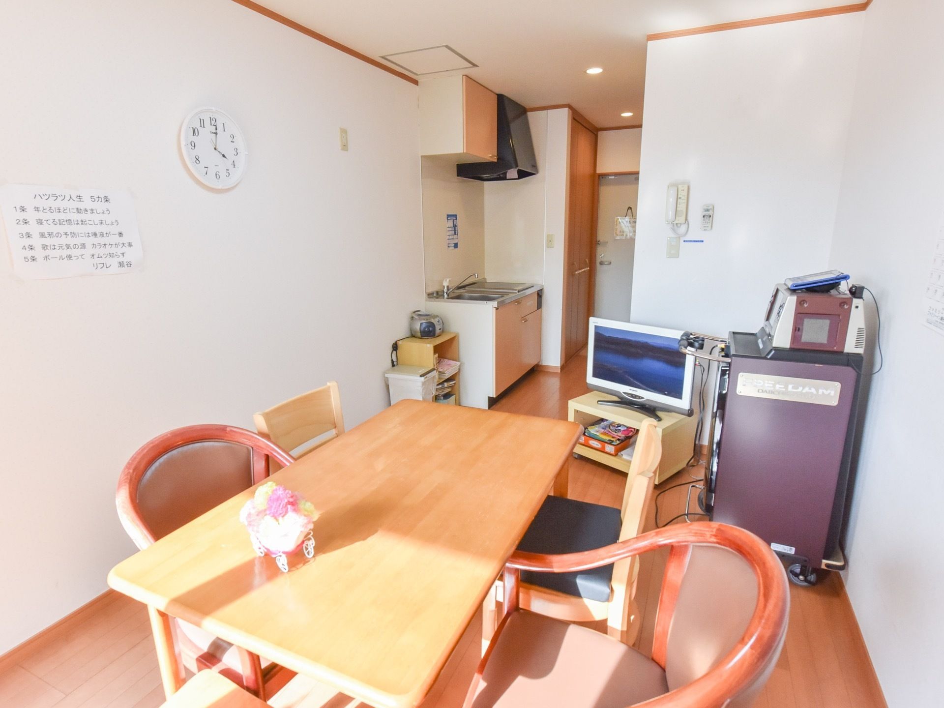 ４人掛けのテーブルと椅子、テレビなどが置かれている。居室のドア付近にはクローゼット、キッチンが並んでいる。