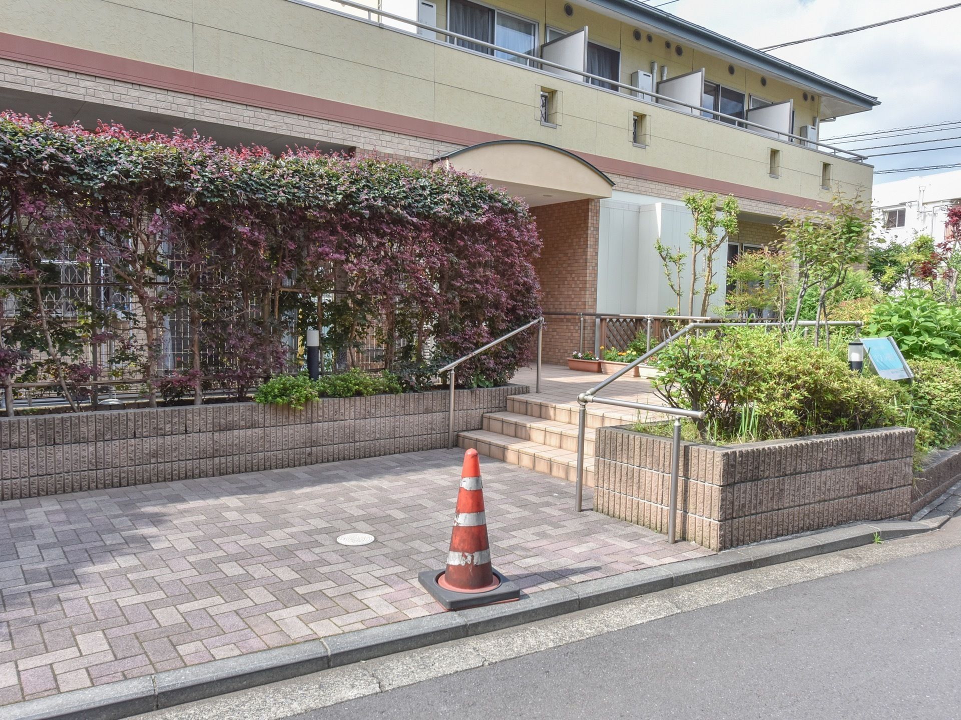 建物と道路の間には一時的に車が止められるスペースが設けられている。玄関に続く階段がある。手すりがついており、昇降をサポートする。