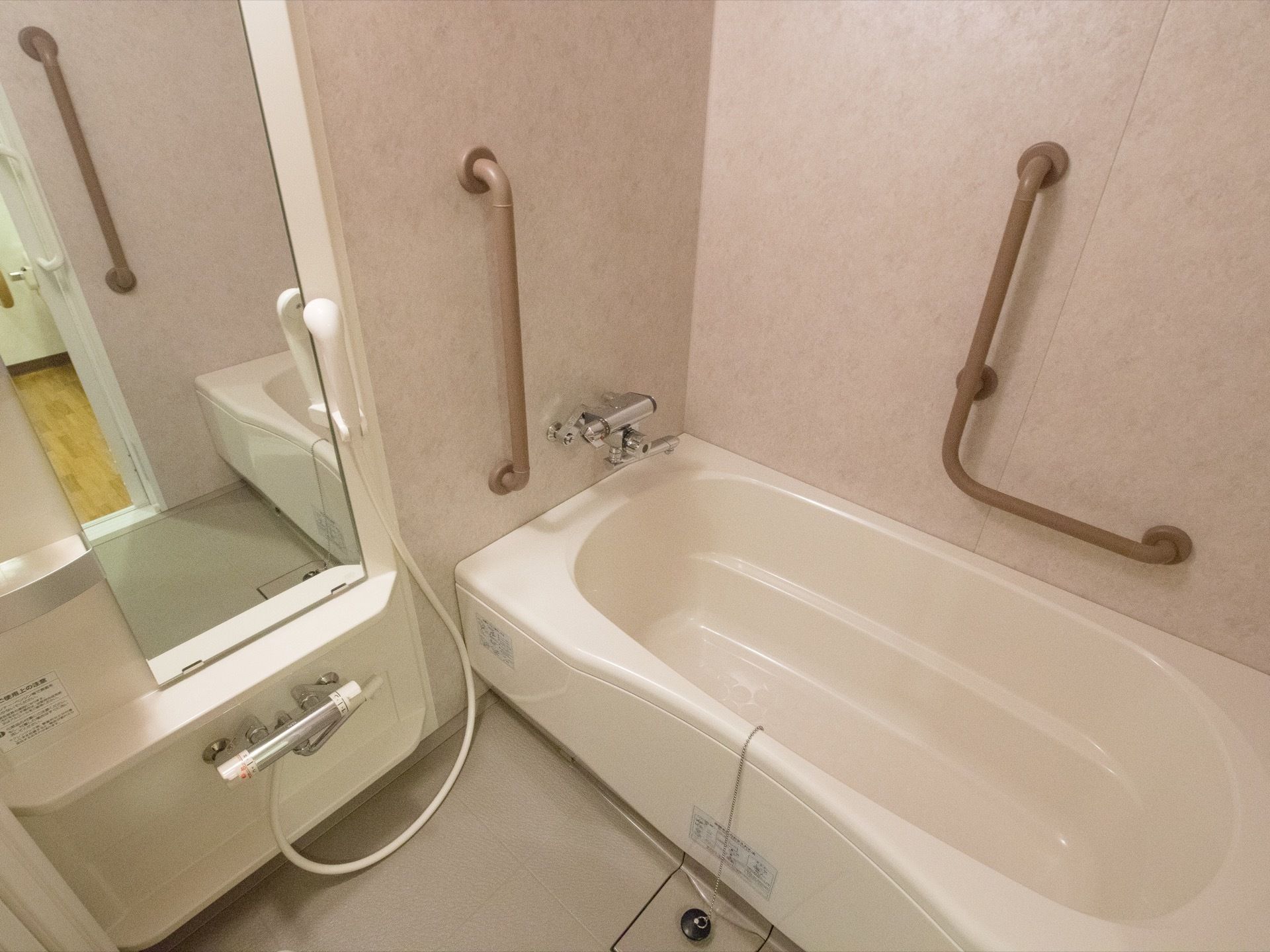 清潔感のある浴室である。浴槽側の壁には薄茶色の手すりが設置されており、入居者様は安全に入浴することができる。