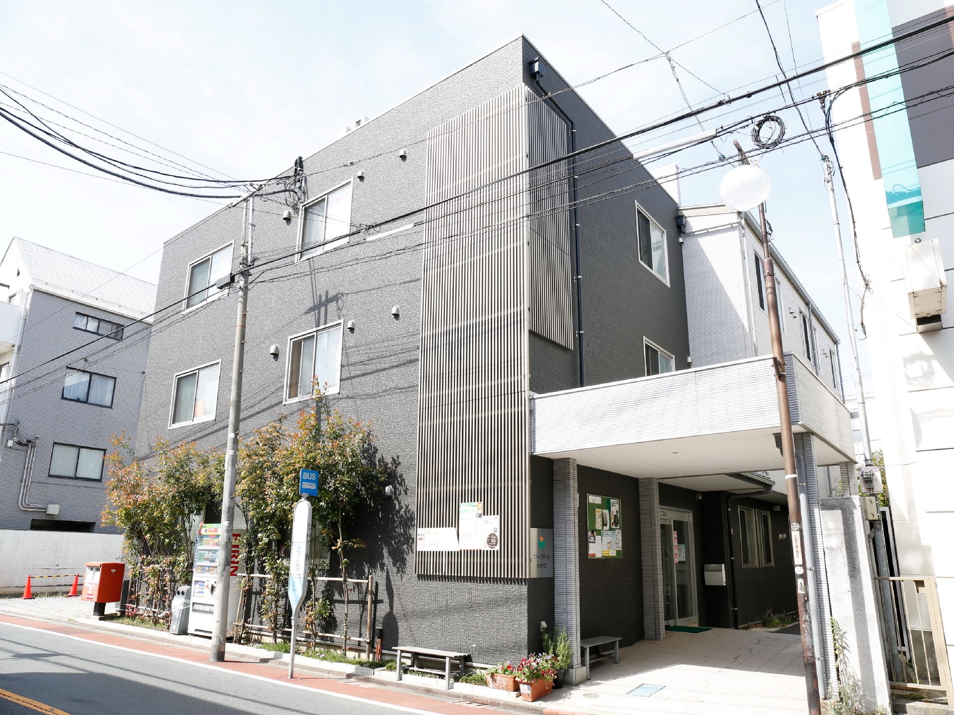 施設はグレーを基調とした建物で、玄関前には大きなひさしが設けられている。ドアの横に掲示板があり、お知らせのチラシなどが貼られている。